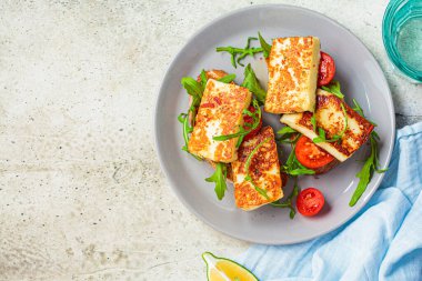 Gri tabakta roka ve domatesli kızarmış halloumi sandviçi. Kızarmış peynir ve domatesli tost.