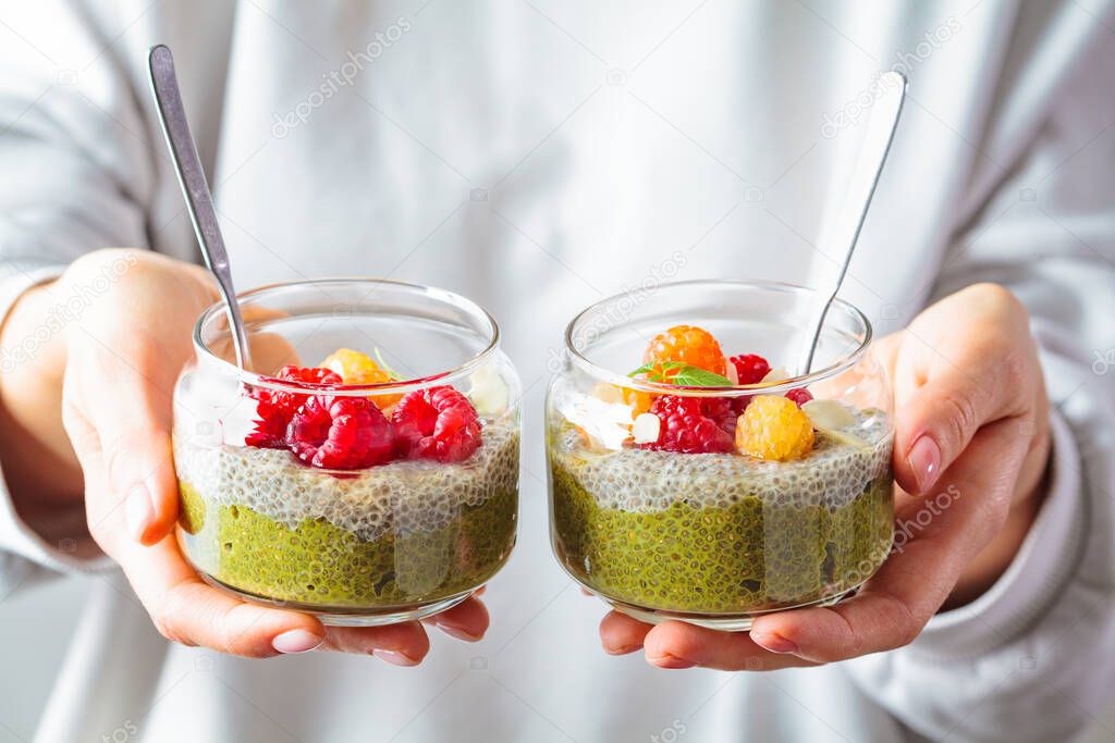 Woman holding chia pudding with matcha tea and berries in a glass jar. Healthy food concept.
