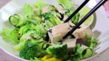 Brokolili yeşil Asya salatası, füme tofu ve fındık soslu beyaz kâse.