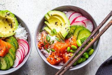 Somon, pirinç, avokado, edamame fasulyesi, salatalık ve turpla dolu gri bir kâse. Hawaii ahi poke kasesi, gri arka plan.