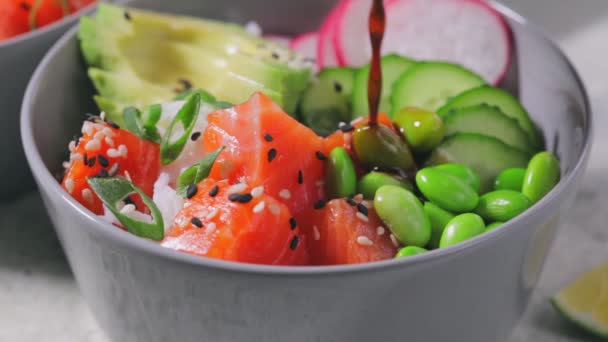 Poke bowl con salmón, arroz, aguacate, judías edamame, pepino y rábano en tazón gris. — Vídeo de stock