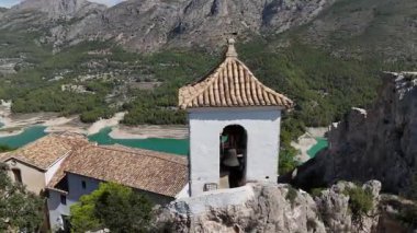 El Castell de Guadalest 'in tarihi çan kulesinin insansız hava aracı görüntüsü. Manzaralı dağlar ve arka planda turkuaz rezervuarı var. Seyahat, turizm, tarih ve mimari projeleri için mükemmel görüntüler.