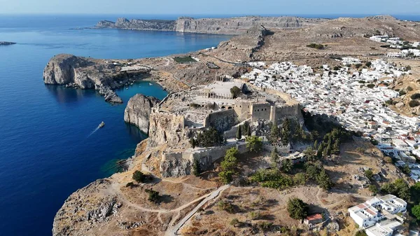 Turkuaz Ege Denizi 'nin, Yunanistan' ın Rodos kıyısı boyunca uzanan geleneksel Yunan evleri ile sarp kayalıklarla buluşmasının çarpıcı insansız hava aracı görüntüleri. Seyahat, turizm ve Akdeniz manzara kavramları için mükemmel..