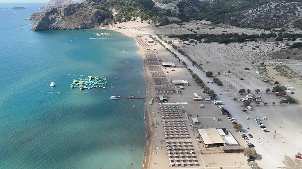 Turkuaz deniz, şişme su kaydırakları ve su üzerinde oyun alanı olan dağlarla çevrili kumlu bir sahil manzarası. Yaz tatili, turizm, aile eğlencesi ve kıyı eğlencesi kavramları için mükemmel..