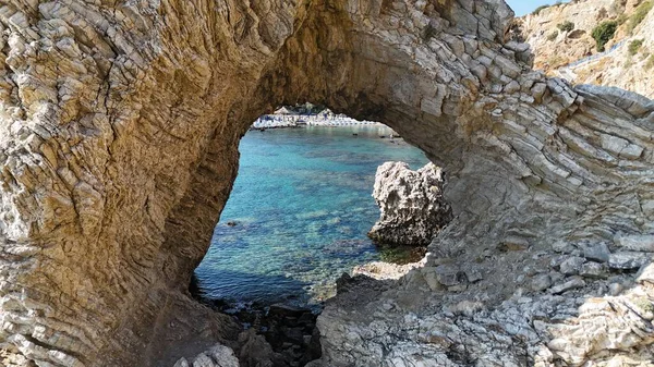 Güneşli bir yaz gününde kristal berrak turkuaz su ve engebeli uçurumların çarpıcı manzarasını çerçeveleyen dramatik sahil kaya kemeri. Seyahat, macera ve doğa temaları için mükemmel.