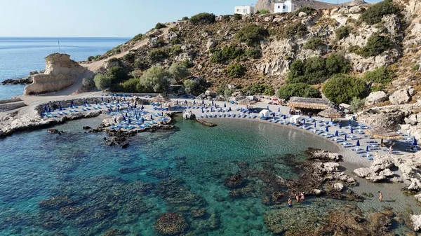 Kayalık uçurumlar ve kristal berrak turkuaz suyla çevrili küçük bir plajın havadan görünüşü, saman güneş şemsiyeleri ve parlak yaz güneşi altında şezlonglar. Seyahat, tatil ve kıyı kavramları için mükemmel.