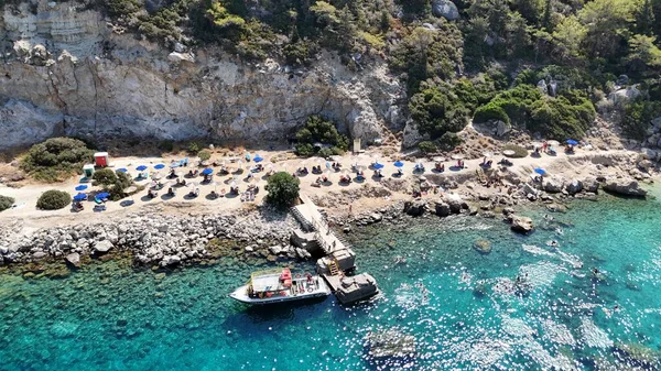 Ünlü Anthony Quinn Körfezi 'nin kristal berrak turkuaz suyuyla drone görüntüsü, saman şemsiyeler ve güneşli bir günde dramatik uçurumlarla çevrili küçük kayalık bir plaj. seyahat, tatil ve doğa kavramları
