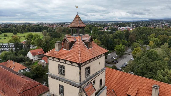 Almanya 'daki Bracke Kalesi' nin çarpıcı görüntüsü, yemyeşil ağaçlar, çimenli çayırlar ve parlak yaz ışığı altında huzurlu bir nehirle çevrili kendine özgü kırmızı çatısını gösteriyor. Seyahat, mimari ve doğa temaları için ideal