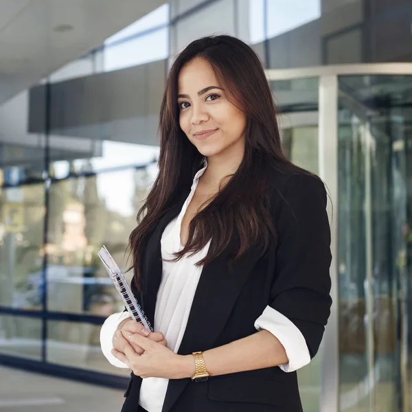 Attractive hispanic young woman in suit holdig a copy book and smiling looking at camera, office manager or teacher