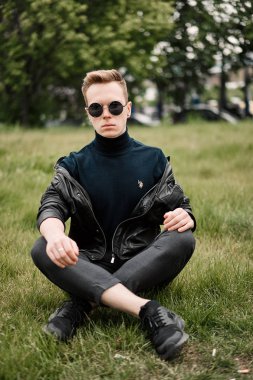 şapkalı adam çimlere oturup güneş gözlüğü takıyor