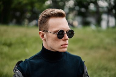 şapkalı adam çimlere oturup güneş gözlüğü takıyor