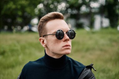 şapkalı adam çimlere oturup güneş gözlüğü takıyor