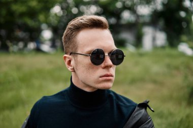 şapkalı adam çimlere oturup güneş gözlüğü takıyor