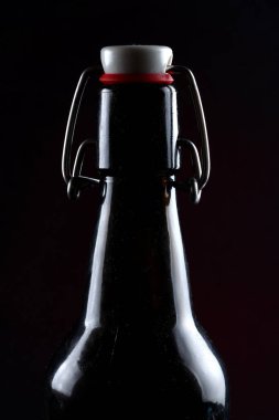 Siyah arka planda kapağı koyu camlı bira şişesi.