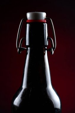 Siyah arka planda kapağı koyu camlı bira şişesi.