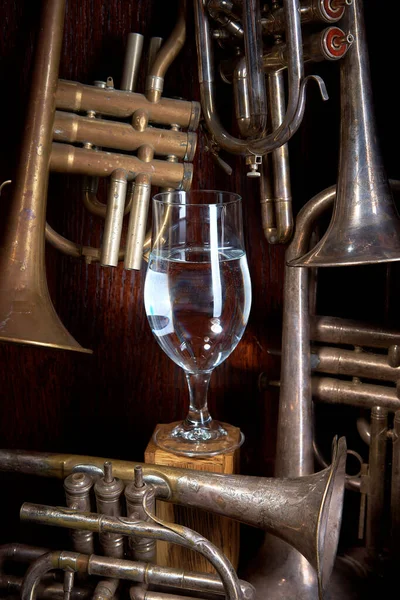 Rör av blåsinstrument på en träbakgrund i mitten av en handske med en ring som håller ett glas med en drink. — Stockfoto