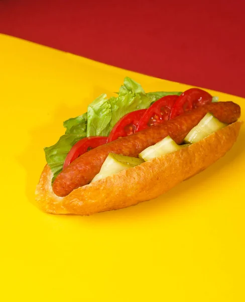 Hot dog on yellow red background bun with sausage salad and cucumber — Stock Photo, Image