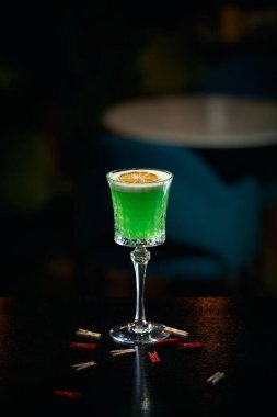 Bardakta yeşil alkollü kokteyl, barın arka planında limon.