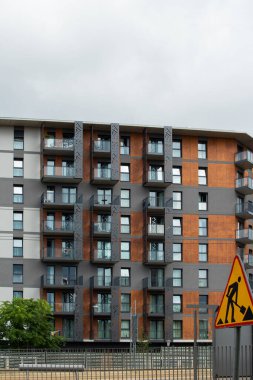 Çağdaş bir apartmanda gri ve ahşap panellerin karışımı sergileniyor. Yapıyı balkonlar süslerken, inşaat tabelası bölgede devam eden gelişmelere işaret ediyor..