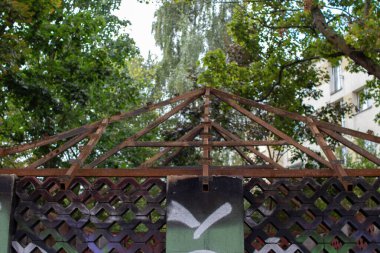 Yıpranmış bir metal yapı, yemyeşil ağaçlar tarafından çerçevelenmiş bir parkta duruyor. Sığınaklar açık tasarım ışığın filtrelemesine izin verirken kentsel öğeler cazibe ekliyor.