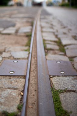 Demiryolu rayları bir kaldırım taşı yolunun yanında görülebilir. Etrafı çimen ve düzgün sıralanmış taşlarla çevrili. Sahne, şehir ulaşımının sakin bir görüntüsünü yakalıyor.