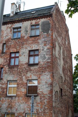 Sakin bir kentsel mahallede yıpranmış bir tuğla bina duruyor. Yapı, yıllar süren ihmal ve geçmişi yansıtan boyalar ve çatlak duvarlara sahiptir..