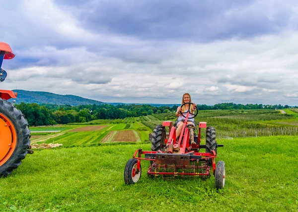 Belle femme sur un tracteur agricole rouge, champ vert, paysage de prairie avec herbe Nord de l'État de New York — Photo