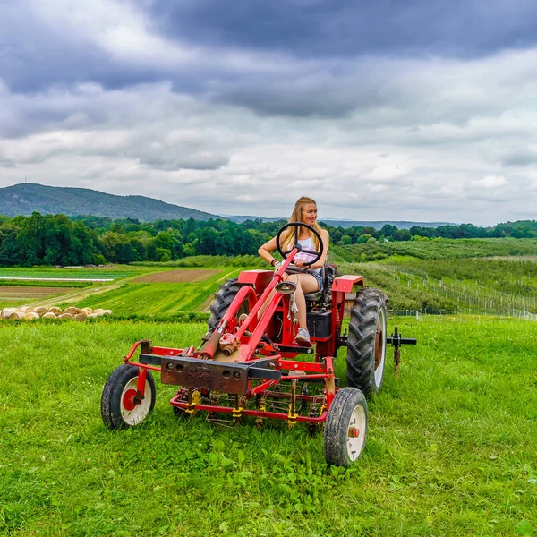 Hermosa mujer en un tractor agrícola rojo, campo verde, paisaje de prado con hierba al norte del estado de Nueva York — Foto de Stock