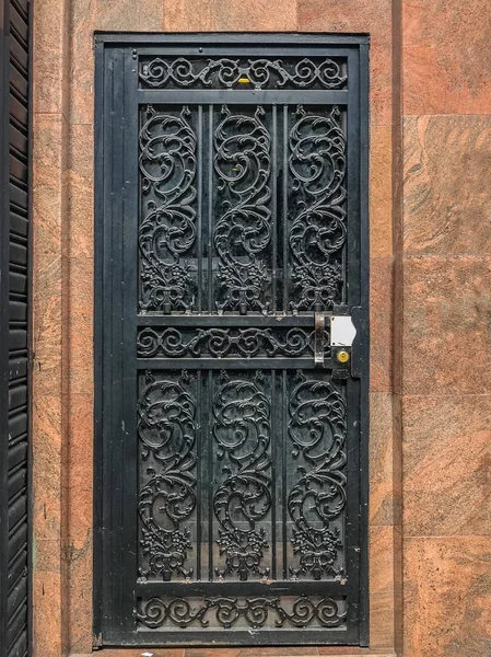 Uma porta antiga em preto com uma textura grande treliça contra o fundo da parede de mármore . — Fotografia de Stock