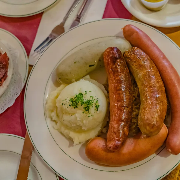 German mixed sausages for beer with mashed potatoes, greens, stewed cabbage and seasonings. — Stock Photo, Image
