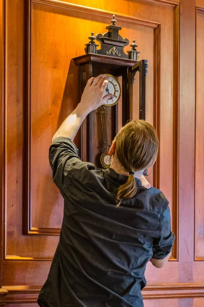 Watchmaker winding up vintage wooden pendulum clock hanging on a wall