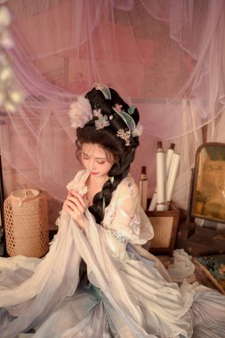 Güzel bir kadın, geleneksel Asya kıyafetleriyle, narin çiçeklerle süslenmiş, kültürel mirasın ve zarif güzelliğin özünü yakalayan, zamansız bir zarafeti simgeler..