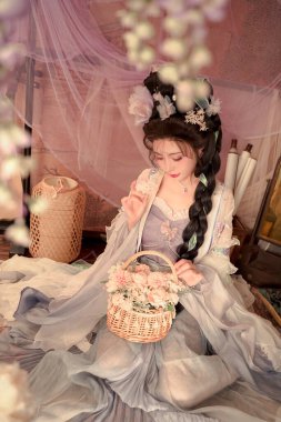 Narin bir el işi elbisesi içinde dingin bir kadın çiçek dolu bir sepet tutar. Işıl ışıl bir güzellik ve zarafet eski moda bir ortamda, manevi ve romantik temalar için mükemmeldir..