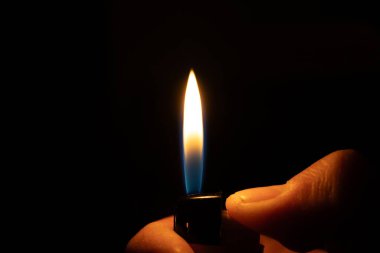 Bir el yanan bir çakmağı tutar, dramatik ve karanlık bir arka plana karşı parlak bir alev üretir..