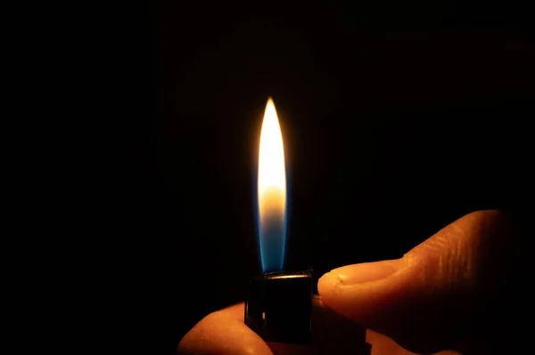 Bir el yanan bir çakmağı tutar, dramatik ve karanlık bir arka plana karşı parlak bir alev üretir..