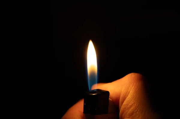 Bir el yanan bir çakmağı tutar, dramatik ve karanlık bir arka plana karşı parlak bir alev üretir..