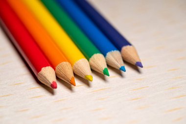 Açık ahşap bir yüzey üzerinde gökkuşağı spektrumunda sıralanmış altı adet sivri uçlu kalem..