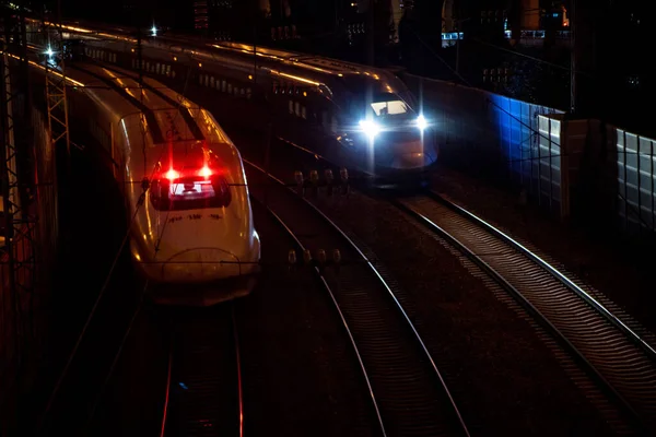 İki yüksek hızlı tren, gece rayların üzerinde birbirlerinin yanından geçerken hareket ve parlak ışıklar görüyorlar..
