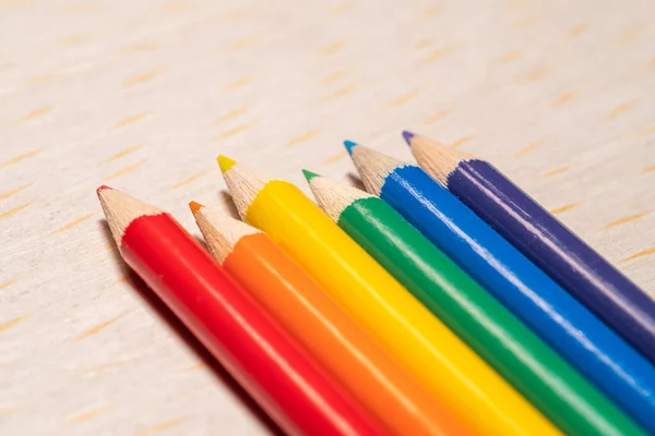 Açık ahşap bir yüzey üzerinde gökkuşağı spektrumunda sıralanmış altı adet sivri uçlu kalem..