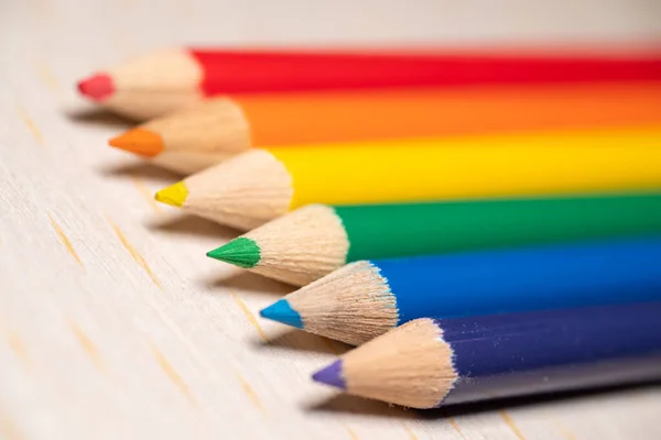 Açık ahşap bir yüzey üzerinde gökkuşağı spektrumunda sıralanmış altı adet sivri uçlu kalem..