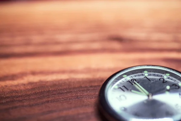 Kahverengi ahşap bir yüzey üzerinde parıldayan elleri olan bir saatin yakın çekim odak noktası..