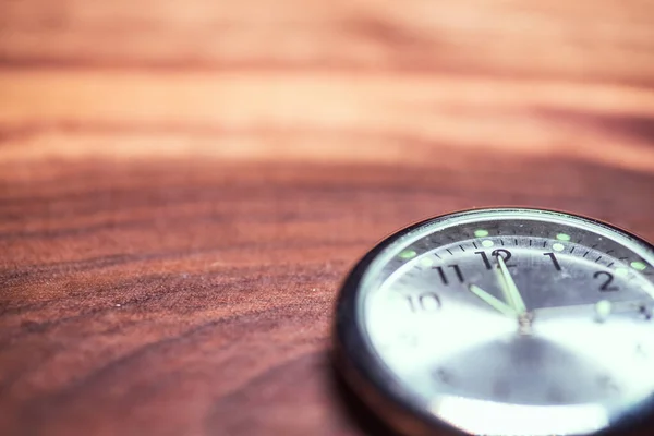 Kahverengi ahşap bir yüzey üzerinde parıldayan elleri olan bir saatin yakın çekim odak noktası..