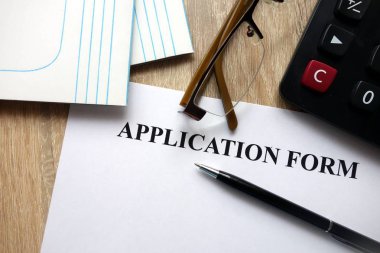 Kalem, hesap makinesi ve masa üzerine gözlük ile başvuru formu