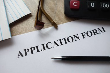 Kalem, hesap makinesi ve masa üzerine gözlük ile başvuru formu