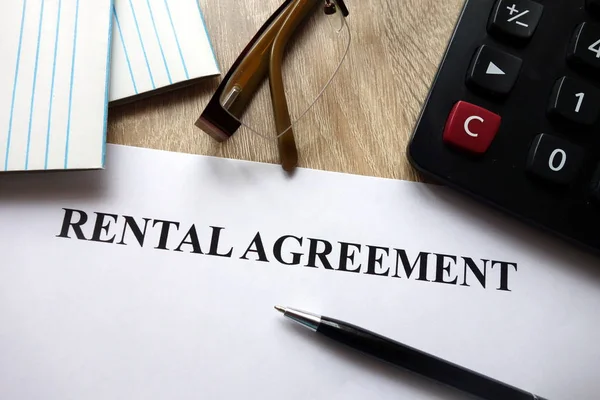 Rental agreement form with pen, calculator and glasses on desk