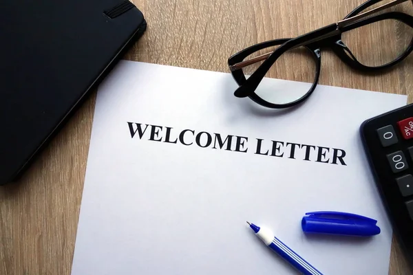 Welcome letter, pen, glasses and calculator on desk
