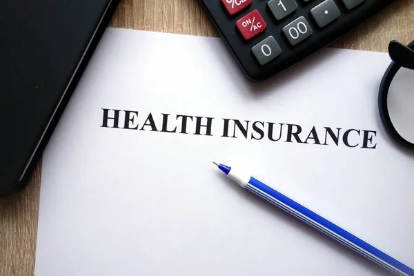 Health insurance document, calculator, pen and glasses on desk