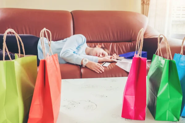 Mujer joven infeliz dormir en el sofá y mantener bolsas de compras con de —  Fotos de Stock