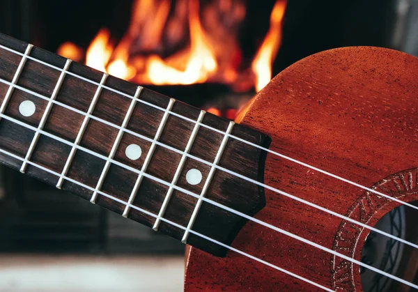 四弦琴小吉他特写刺痛 壁炉上的背景 音乐概念 吉他烦恼板宏 火在烟囱 舒适的浪漫气氛 — 图库照片
