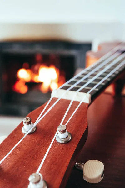 四弦琴小吉他特写刺痛 壁炉上的背景 音乐概念 吉他烦恼板宏 火在烟囱 舒适的浪漫气氛 — 图库照片